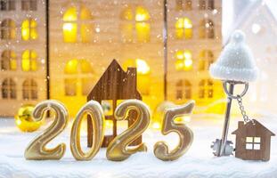 Golden figures number 2025, key and tiny home on background of cozy windows of a house with warm light with festive decor of stars,snow and garlands. Greeting card, Happy New Year, cozy home photo