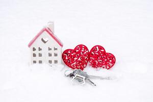 Keys of tiny house and two hearts in snow - Valentine's Day, love in home. Couple housing, real estate, rent, mortgage, relocation. Comfort and warmth in love nest. photo