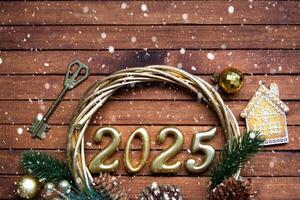 New Year House key with keychain cottage on festive brown wooden background with number 2025 in wreath, lights of garlands. Purchase, construction, relocation, mortgage, insurance photo