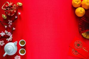 Chinese new year background concept with tea set, ingots word means wealth, red bag, oranges and red envelope packets or ang bao word means blessing and 5 blessing on red satin cloth background. photo