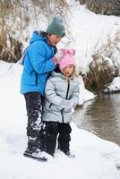 A boy and a girl play in a snow-covered park on the riverbank. A photo of a kids in a winter forest. Winter, winter holidays, vacation holidays.