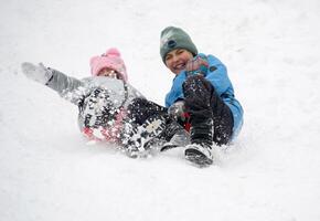 A girl and a boy in a snowy forest are riding an ice slide down a slide. Photo of a child in a winter forest. Winter, winter holidays, vacations, vacations.