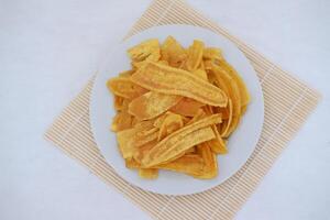 Crispy banana chips on a white plate with fresh bananas. photo