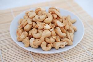 Roasted cashew nuts in white bowl on bamboo mat, stock photo