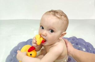 linda 8 mes antiguo niña se baña en un bañera con patitos foto