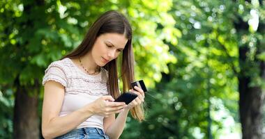 SPortrait of a happy woman paying online with credit card and smart phone in a park photo