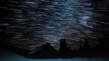 Wooden house in the mountains in winter. Time lapse of Star trails in the night sky. 4K video