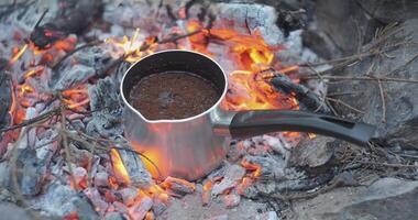 Preparing coffee on coals in a coffee maker. Brewing coffee on a campfire in nature, close-up. Travel concept. 4k video