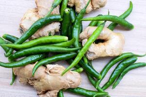 Fresh Ginger and green chili pepper on plain wooden table, green essential vegetables for all essential foods, view of unpeeled vegetables with plain background photo