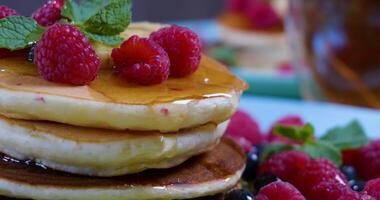 Closeup of Pouring honey on stack of pancakes. Tasty breakfast food. Pancakes are served with raspberries, banana and mint leaf. Ultra 4K video