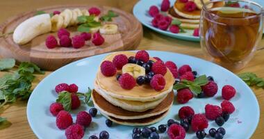 Sweet honey pouring over pancakes. Tasty breakfast food. Pancakes are served with raspberries, banana and blueberry. Honey dripping down on dessert. Ultra 4K video