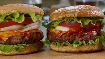 Frais appétissant du boeuf des hamburgers sur le cuisine tableau. délicieux Burger avec Frais iceberg chou, oignons, tomates et grillé steak. vite nourriture, Piste caméra mouvement, 4k video