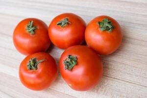 Red tomato on plain wooden table, essential vegetables for all essential foods, view of unpeeled vegetables with plain background photo
