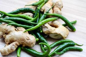 Fresh Ginger and green chili pepper on plain wooden table, green essential vegetables for all essential foods, view of unpeeled vegetables with plain background photo