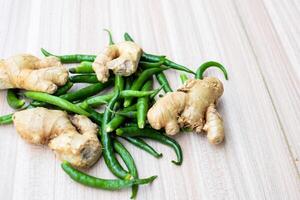 Fresh Ginger and green chili pepper on plain wooden table, green essential vegetables for all essential foods, view of unpeeled vegetables with plain background photo