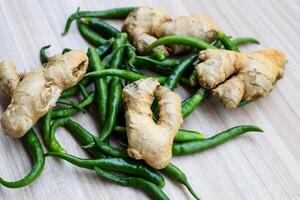 Fresh Ginger and green chili pepper on plain wooden table, green essential vegetables for all essential foods, view of unpeeled vegetables with plain background photo