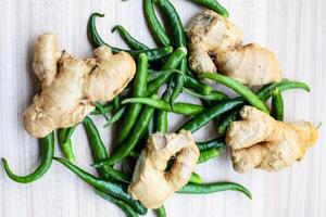 Fresh Ginger and green chili pepper on plain wooden table, green essential vegetables for all essential foods, view of unpeeled vegetables with plain background photo