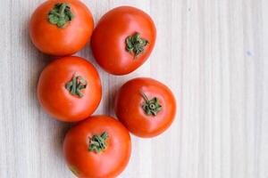 Red tomato on plain wooden table, essential vegetables for all essential foods, view of unpeeled vegetables with plain background photo