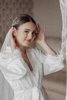 The bride in a silk suit and veil poses in her room. Morning of the bride. Preparation. Wedding photography photo