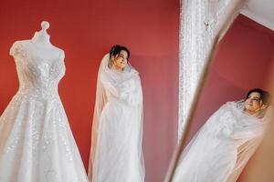 portrait of a luxurious bride in boudoir style near a mirror with reflection. Preparing the bride for the wedding in the morning in a white robe. photo