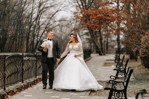 The bride and groom are walking near the hotel and posing, happy and enjoying the day, holding hands. A long train on the dress. Winter wedding photo