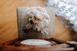 hogar estilo. Boda ramo de flores de crema y rosado flores en un silla a hogar debajo luz. detalles de el novia y novio. foto