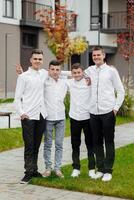 Group of smiling and happy teenage friends wearing casual clothes spending time together, posing and talking with each other near college building on autumn day. photo