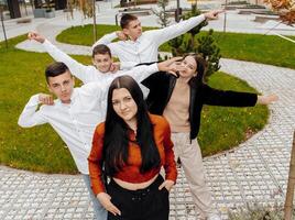 un grupo de sonriente y contento Adolescente amigos, vestido en casual ropa, gastar hora juntos, actitud y tener divertido en el jardines de un educativo institución en un otoño día. foto