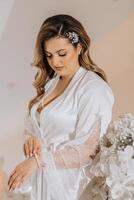 Morning of the bride before the wedding. A beautiful young woman with a veil and a beautiful hairstyle in a white robe in a room with a wonderful interior. Natural beauty and professional makeup. photo