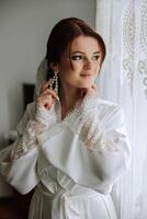 A beautiful brunette bride with a tiara in her hair is getting ready for the wedding in a beautiful robe in boudoir style. Close-up wedding portrait, photo. photo