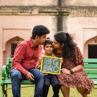 Indian couple posing for maternity baby shoot with their 5 year old kid. The couple is posing in a lawn with green grass and the woman is flaunting her baby bump in Lodhi Garden in New Delhi, India photo
