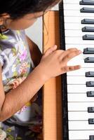 Asian cute girl playing the synthesizer or piano. Cute little kid learning how to play piano. Child's hands on the keyboard indoor. photo