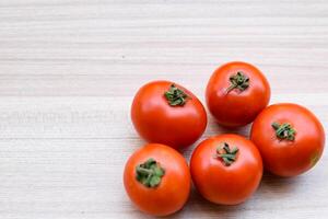 Red tomato on plain wooden table, essential vegetables for all essential foods, view of unpeeled vegetables with plain background photo