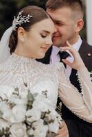 A bride in a long dress and a groom in a black suit are standing near white Roman-style columns. Beautiful hair and makeup. An exquisite wedding photo