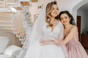 A friend helps the bride fasten her dress. A woman helps her friend fasten the buttons on the back of her wedding dress. The morning of the bride, the creation of a family, an important event. photo