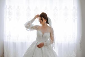 fashion photo of a beautiful bride with dark hair in an elegant wedding dress and stunning makeup in the room on the morning of the wedding. The bride is preparing for the wedding