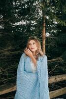 portrait of a cute bride with a wreath on her head, she is wrapped in a blue blanket against the background of a winter forest. Winter wedding. photo