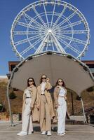 Three beautiful young teenage girls having fun together outdoors against the background of a ferris wheel in an Italian town. Urban lifestyle. City center. Best friends in casual clothes. photo