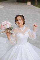 brunette bride in off-the-shoulder lace white dress and tiara posing with a bouquet of white and pink flowers. Beautiful hair and makeup. Spring wedding photo