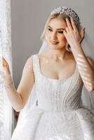 The bride in a white dress, veil poses in beautiful lighting in her room. Morning of the bride. A beautiful tiara photo