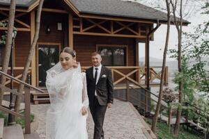 Portrait. A bride in an elegant long dress and veil and a groom in a suit pose while standing near trees. Wedding in nature photo