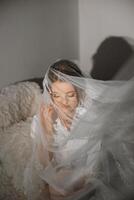 Nice cute girl in a boudoir robe. Happy beautiful bride under veil closeup. Fashion, beauty, style. Morning of the bride. Beautiful bride with stylish make up and hair style. photo