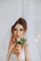 A luxurious bride with a beautiful hairstyle and a gorgeous dress is getting ready for the wedding ceremony in the morning. Morning photo of the bride at home or in a hotel room. Professional makeup.