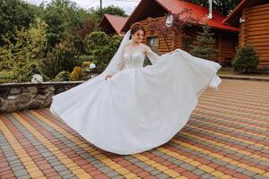 A red-haired bride is circling in her wedding dress, against the background of mountains and wooden houses. Magnificent dress with long sleeves, open bust. photo