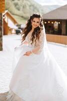 Curly bride twirls in her wedding dress. Magnificent dress with long sleeves, open bust. Summer wedding photo