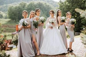 Group portrait of the bride and bridesmaids. A bride in a wedding dress and bridesmaids in silver dresses hold stylish bouquets on their wedding day. photo