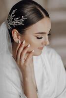 The bride in a silk suit and veil poses in her room, sitting on the couch. Morning of the bride. Preparation. Wedding photography photo