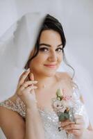 fashion photo of a beautiful bride with dark hair in an elegant wedding dress and stunning makeup in the room on the morning of the wedding. The bride is preparing for the wedding