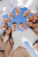 Large group of smiling young people standing, hugging, looking at camera. Group of cheerful teenage people in a circle looking down. Low viewing angle. Copy space. photo