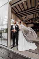 linda recién casados son suavemente abrazando y sonriente cerca el restaurante. retrato de el novia y novio en un cordón vestido. foto